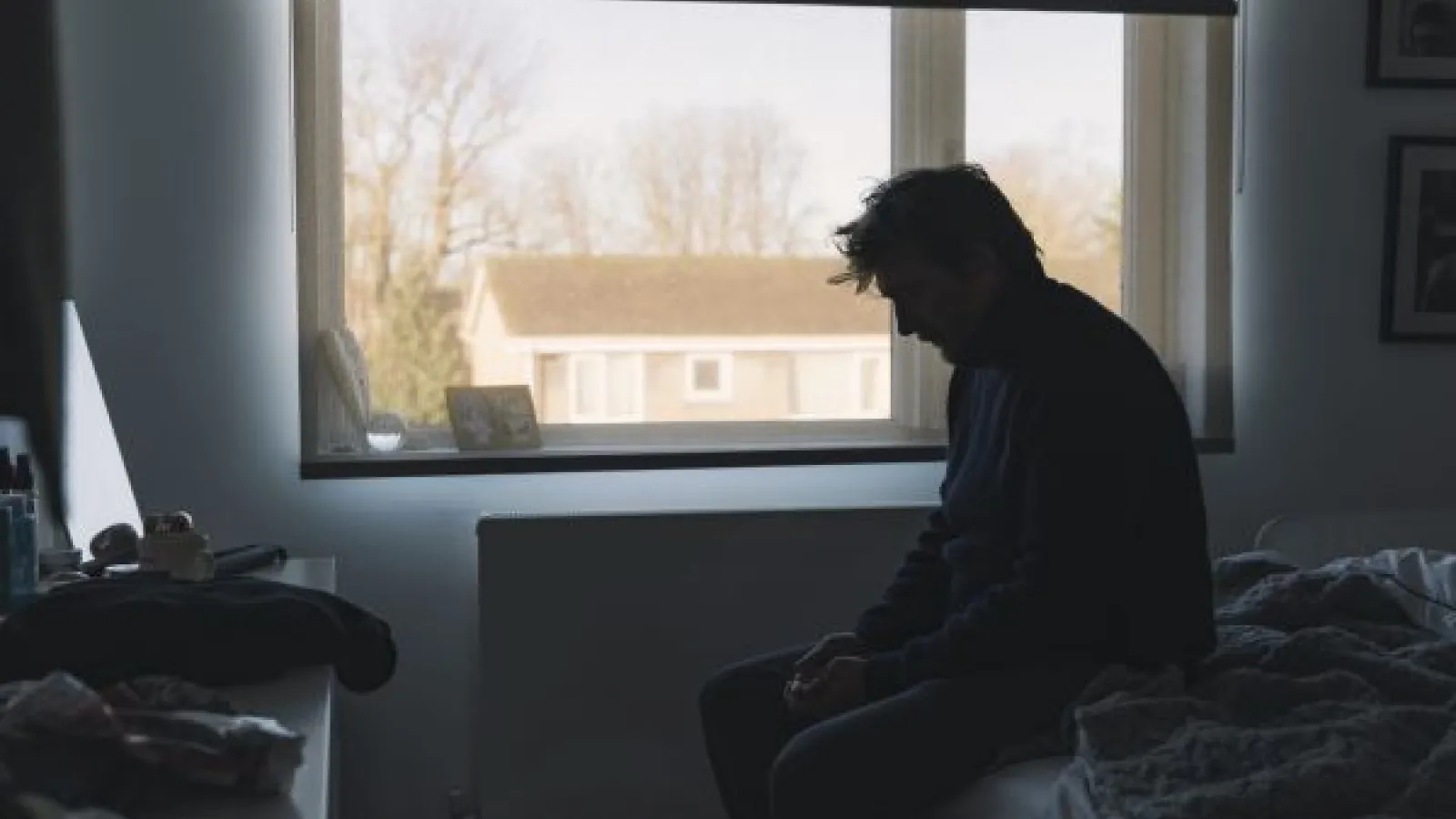a man sits on a bed, head down and obviously sad