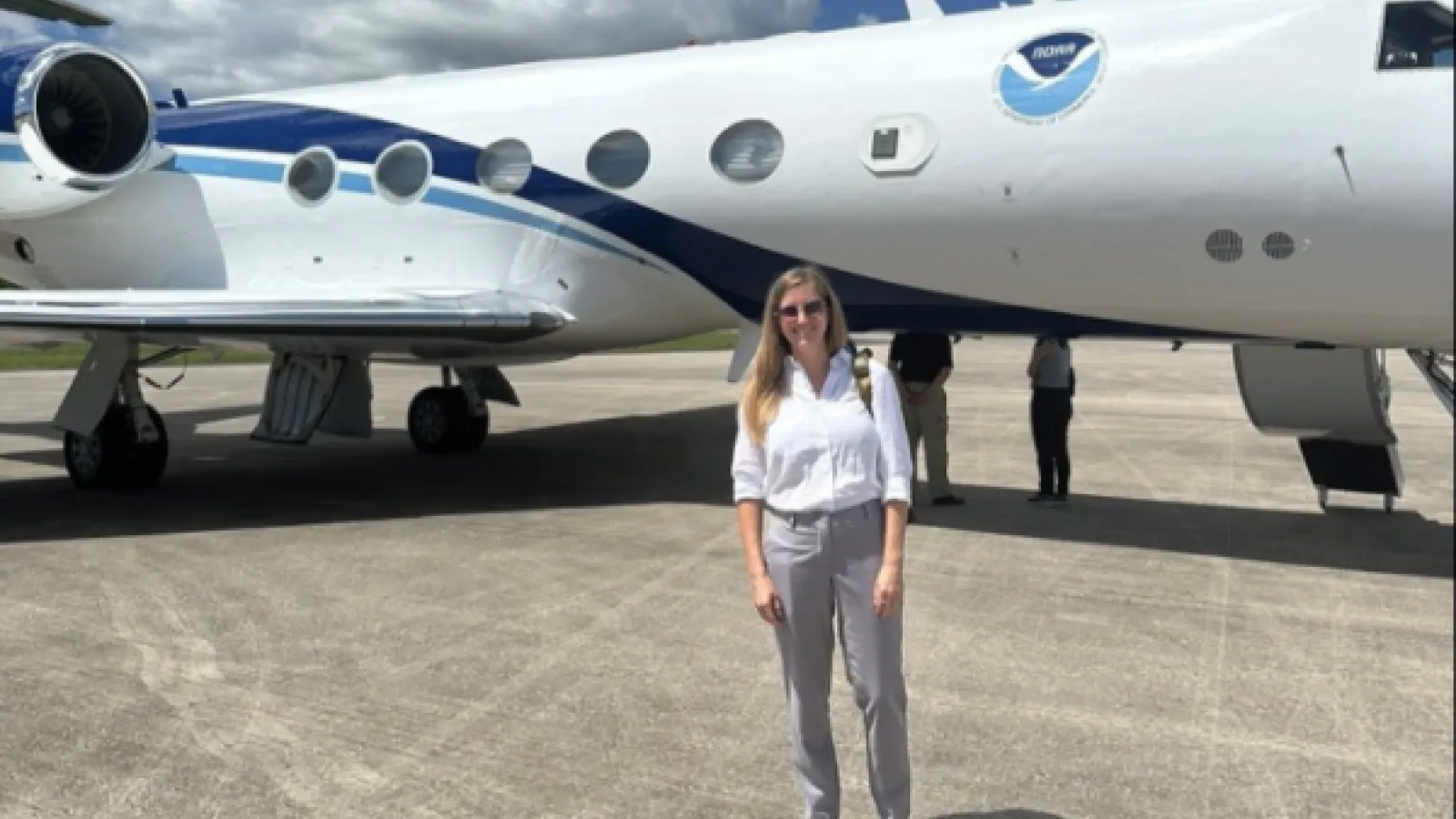 a young woman stands in front of a NOAA plane