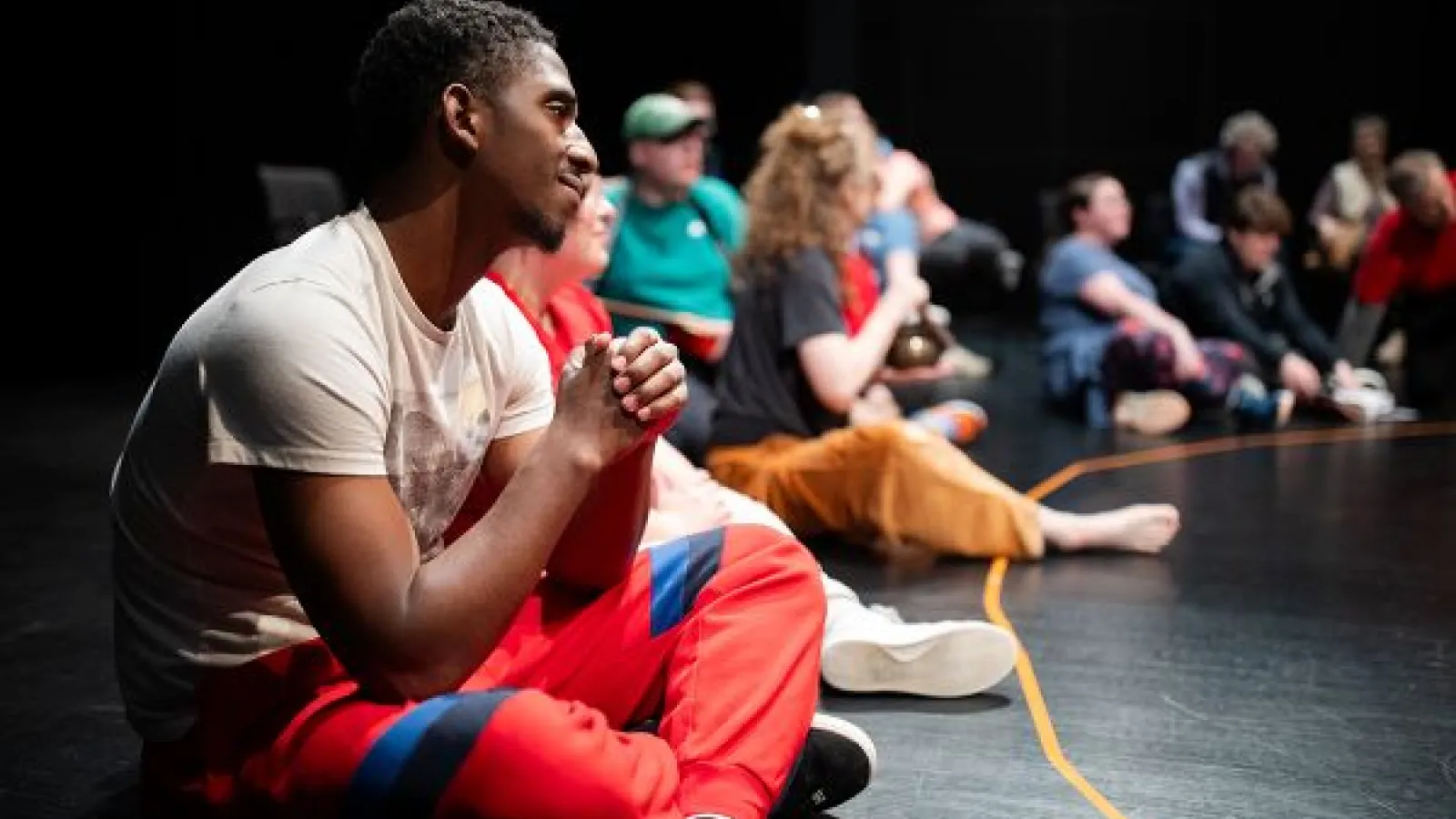 a young man sits on a stage floor, smiling