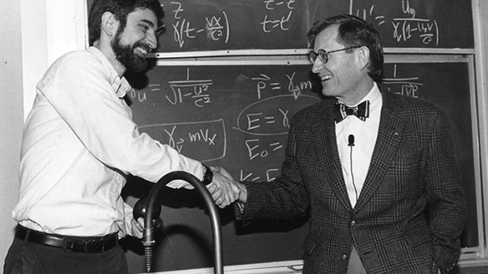 A professor and E. Gordon Gee shake hands in front of a blackboard filled with math equations.