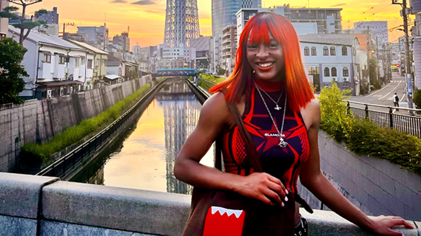 A student with bright red hair smiles on a bridge in Taiwan