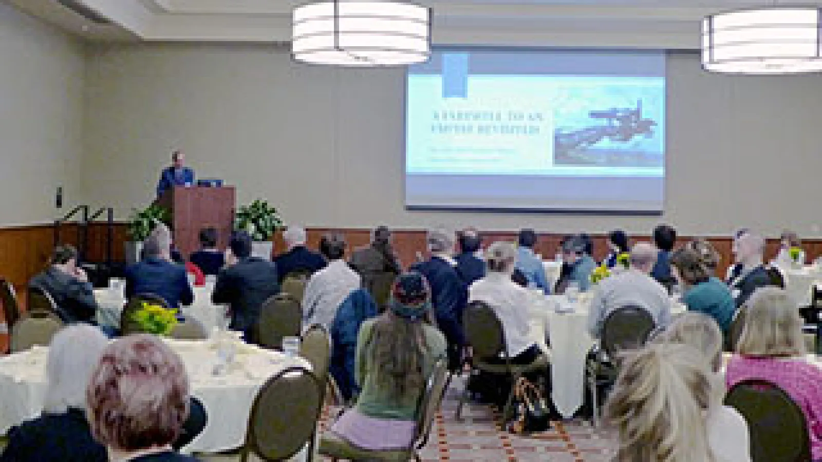 People sitting at circular tables and listening to a keynote speaker
