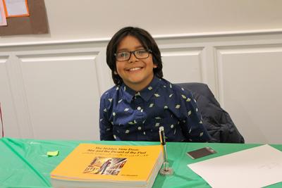 A child poses with his published book about heritage