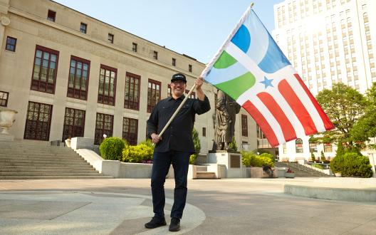 Professor of design Paul Nini waves The People's Flag of Columbus in front of Columbus City Hall. Photo courtesy of Brian Kaiser.