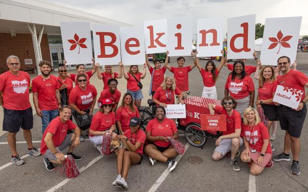 A group of volunteers in red shirts with a sign reading "be kind"
