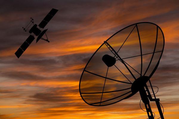 Satellite dish and satellite in front of a sunset