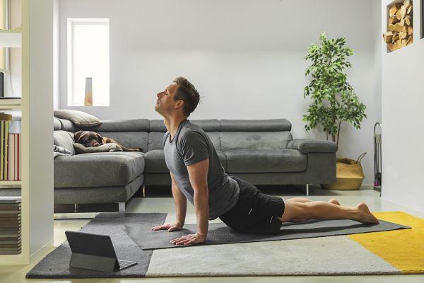man doing yoga while a dog watches from the couch