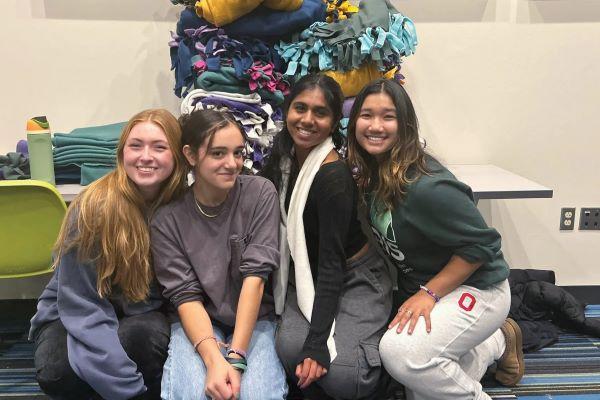 four students pose for the camera in front of a pile of fleece blankets