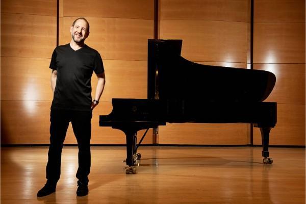 Don Berman stands on a stage in front of a piano