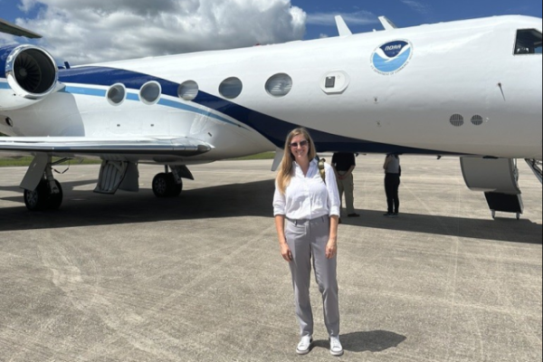 a young woman stands in front of a NOAA plane