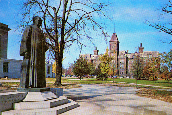 A postcard of the Thompson statue with University Hal behind it. 
