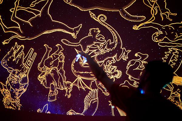 A student in shadow points up to astrology symbols projected onto the ceiling.