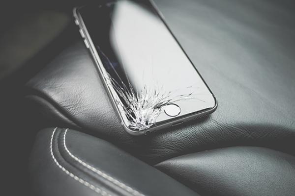 A cellphone with a cracked screen sits on a car seat